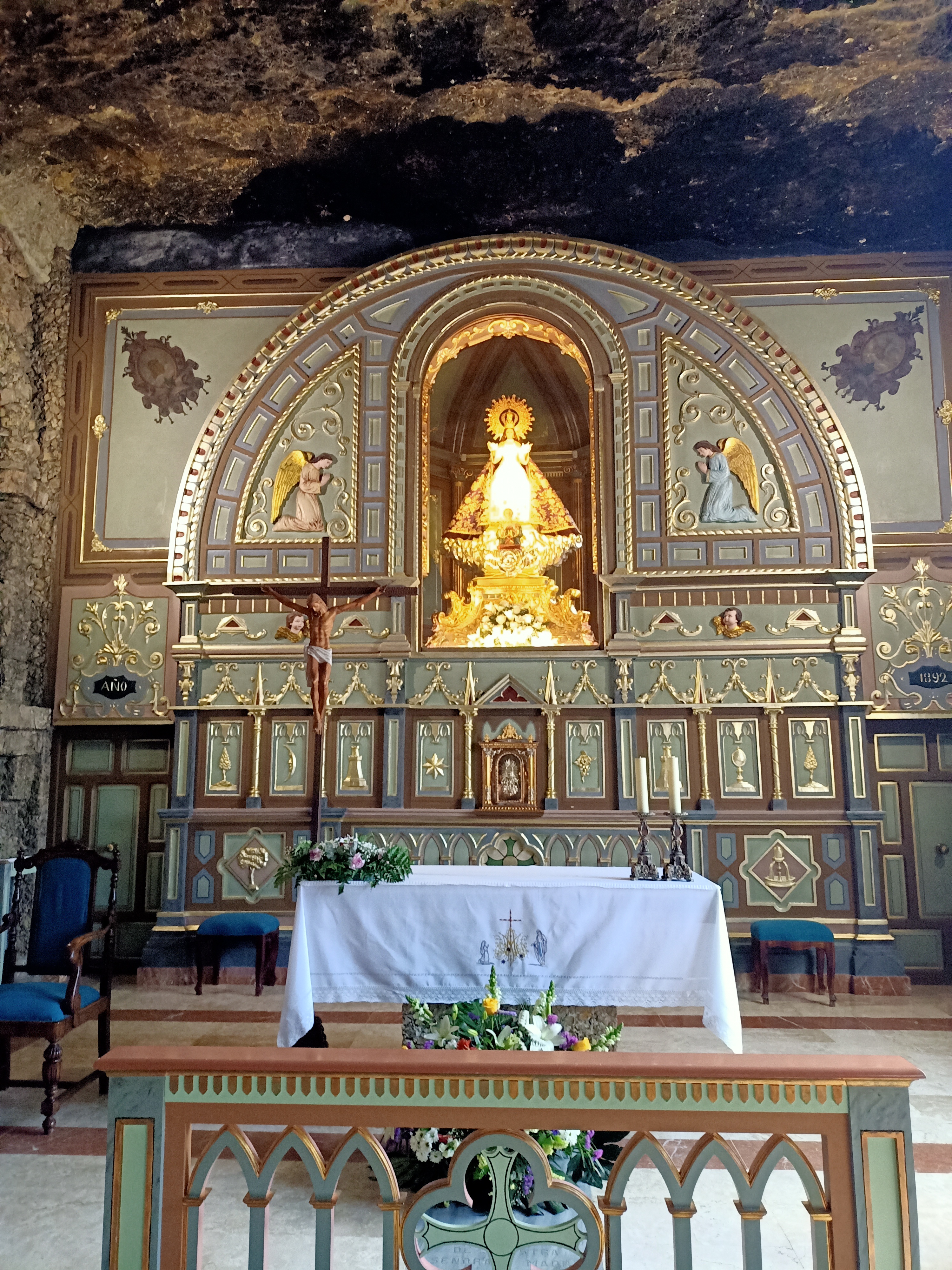 Kuvassa kallioon louhittu kirkon alttari, jossa keskellä kultainen neitsytpatsas kaarevan holvin keskellä.