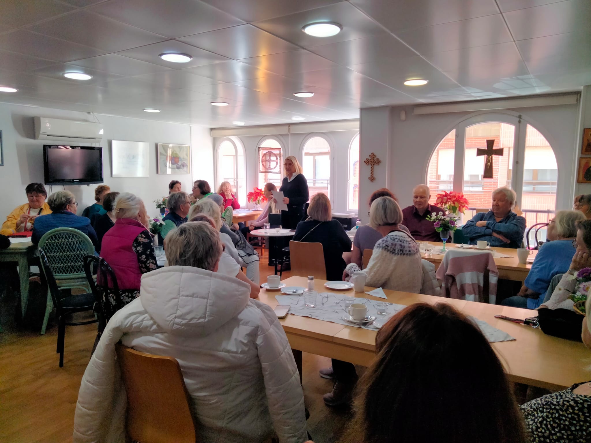 Kuvassa seurakuntakodin valoisassa kahviossa on paljon naisia ja muutama mieskin kuuntelemassa päivän luenn...